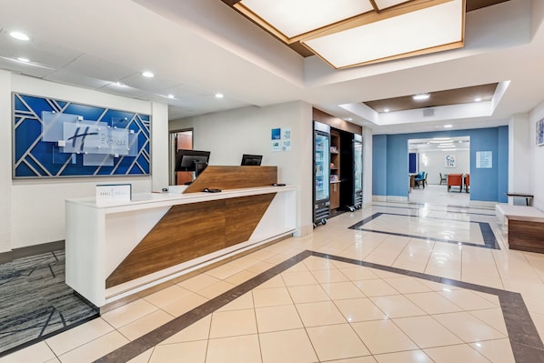 Uma área de recepção de hotel com design moderno, incluindo um balcão de atendimento, uma parede azul com padrão geométrico e piso em azulejos.
