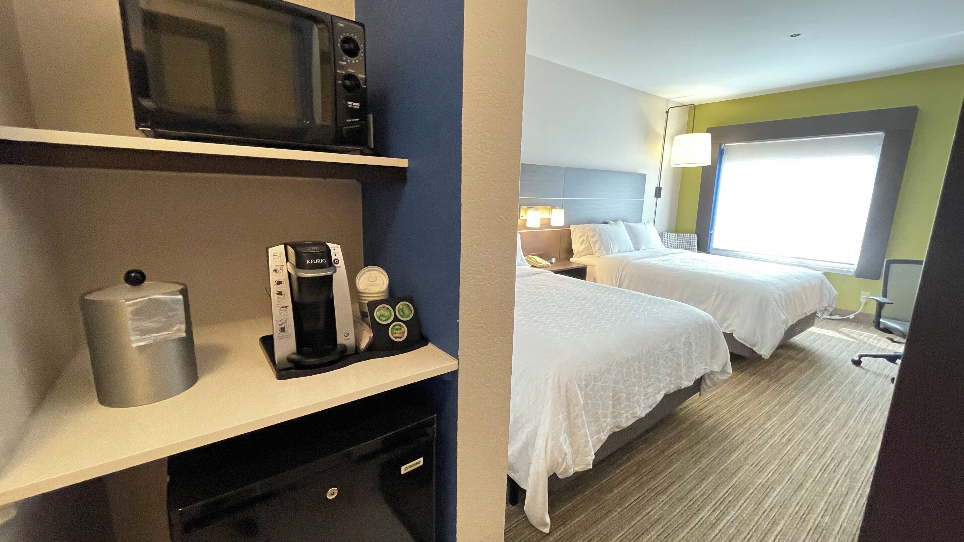 A hotel room with a kitchenette, a bed, a desk with a coffee maker, and a window with a view.