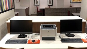 Ett modernt kontorsutrymme med två skrivbord, var och en utrustad med en datorskärm, ett tangentbord och en mus. En skrivare står i mitten av rummet. Rummet har en whiteboard, en soffa och konstverk på väggarna.