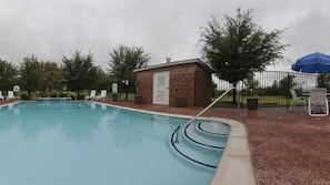 A swimming pool with a brick building, lounge chairs, and an umbrella.