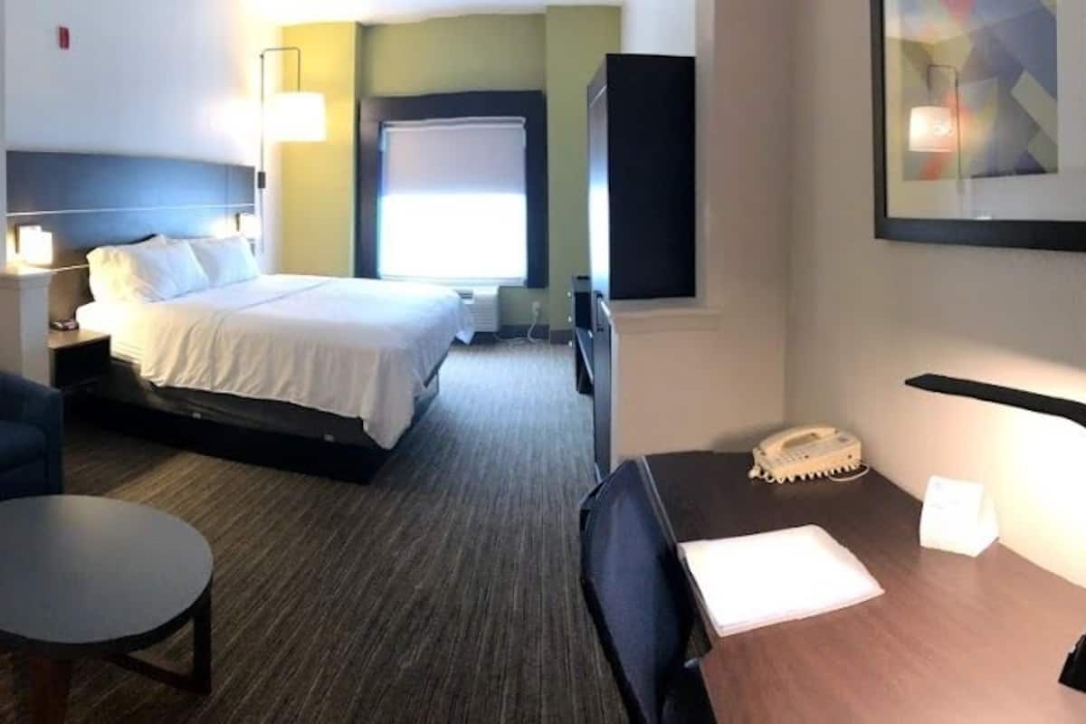 A hotel room with a bed, a sofa, a small table, a desk with a telephone, and a lamp.