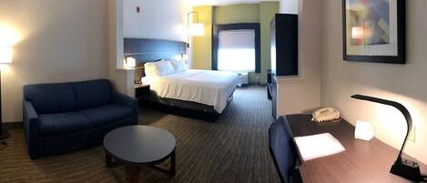 A hotel room with a bed, a sofa, a small table, a desk with a telephone, and a lamp.