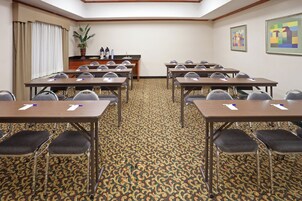 Un salón de conferencias con varias mesas y sillas, una kitchenette y una alfombra estampada.