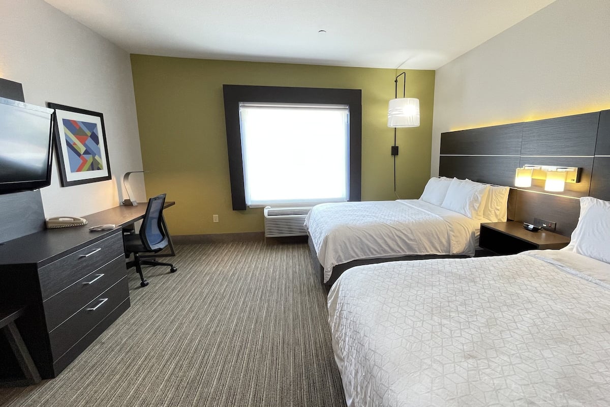 A hotel room with two beds, a desk with a chair, a television, and a window with a view.