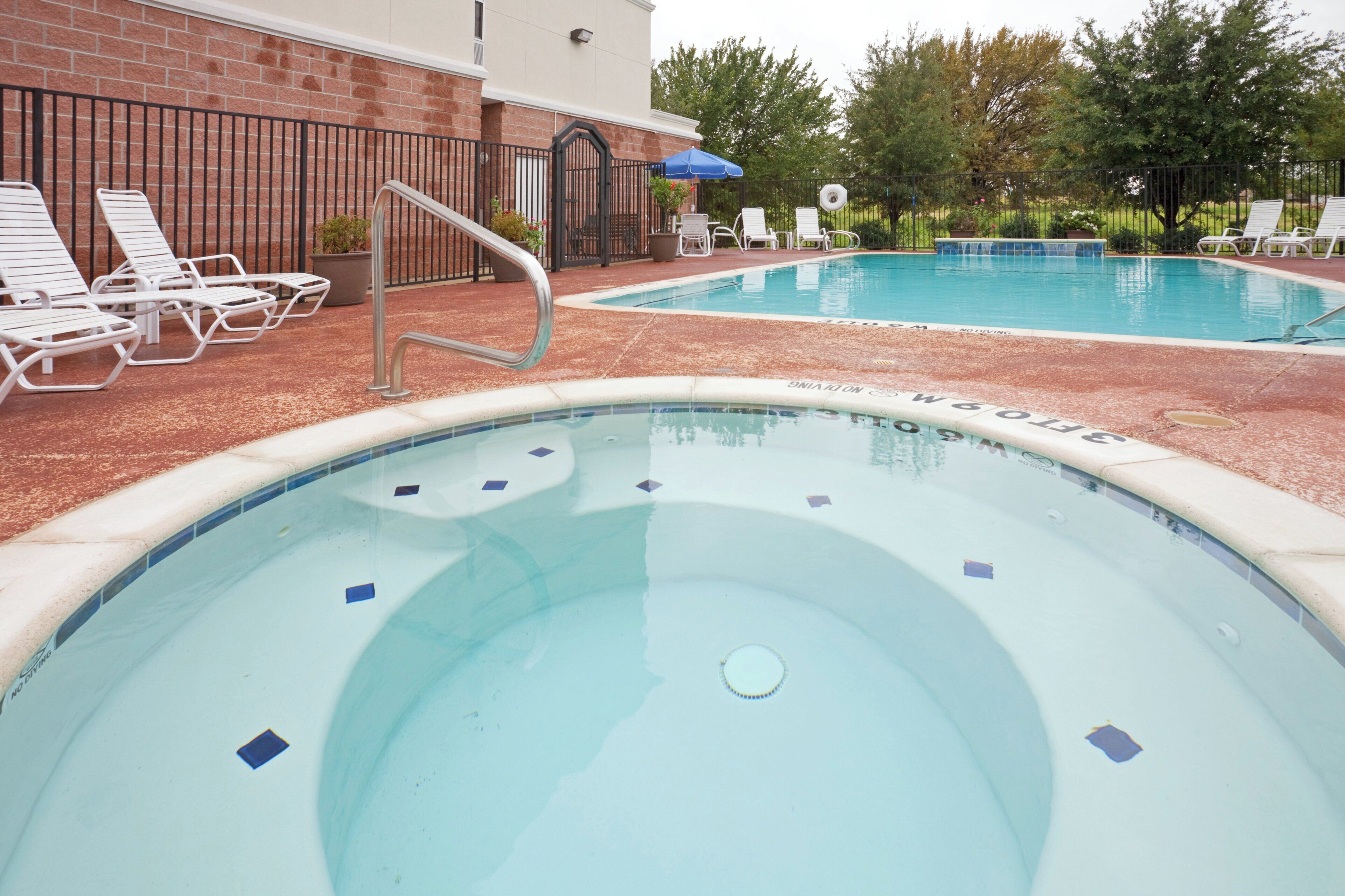A swimming pool with a tiled edge, lounge chairs, and a brick wall in the background.