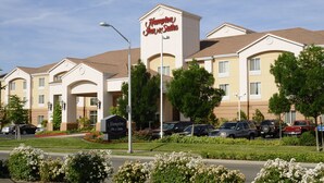 A Hampton Inn & Suites hotel with a beige facade, multiple parking spaces, and a well-maintained lawn.