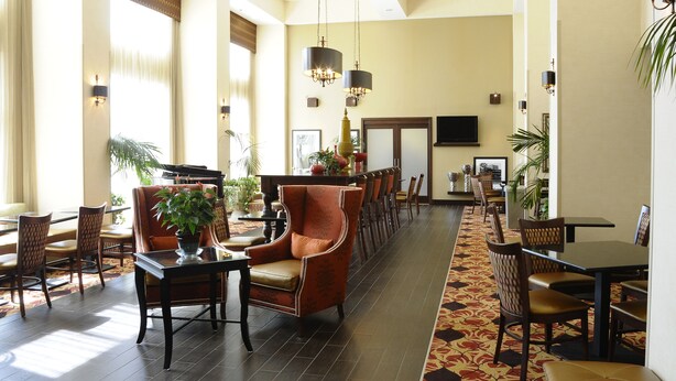 A spacious hotel lobby with a long reception desk, multiple seating areas, and a large TV screen.