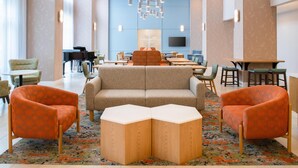 A modern hotel lobby with a central seating area, a piano, and a television on the wall.
