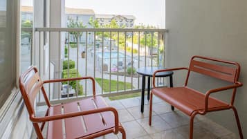 Un balcón con dos sillas de metal y una mesa redonda pequeña, con vista a una piscina y edificios residenciales.