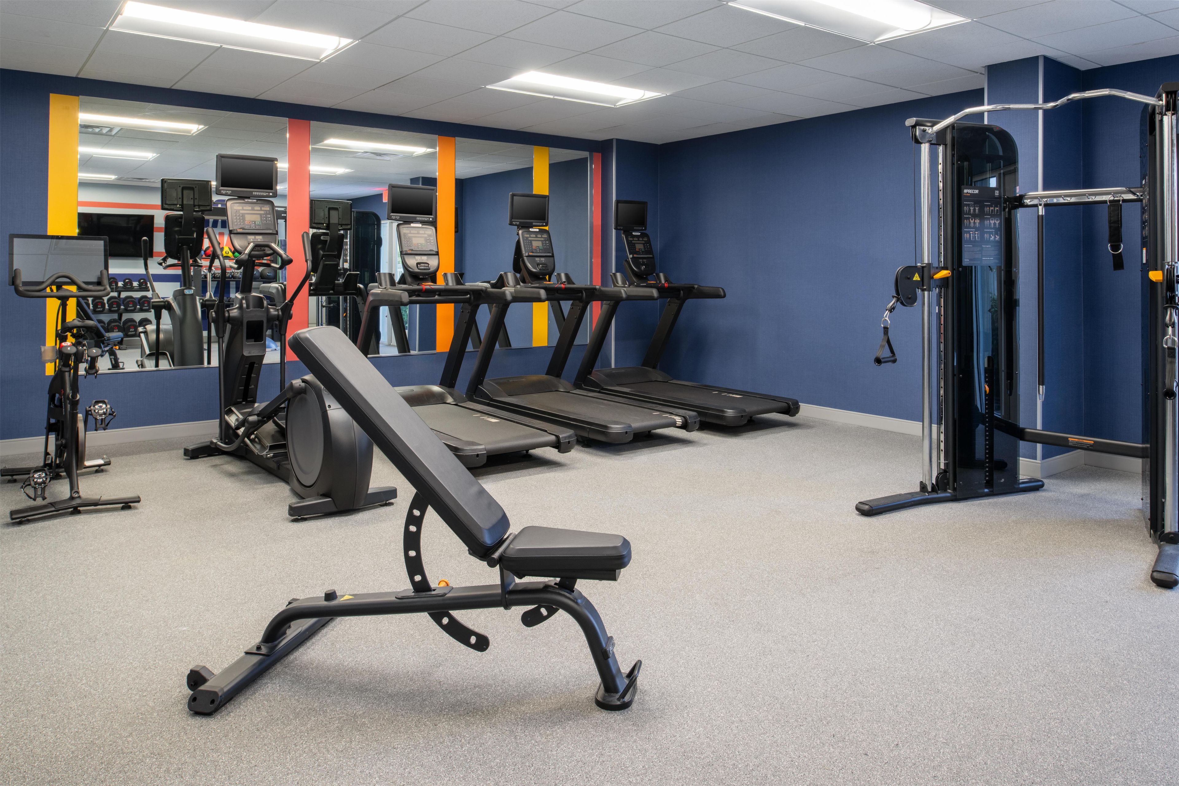 Et fitnesscenter med løbebånd, styrkemaskiner og bænk.