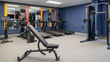 Et fitnesscenter med løbebånd, styrkemaskiner og bænk.