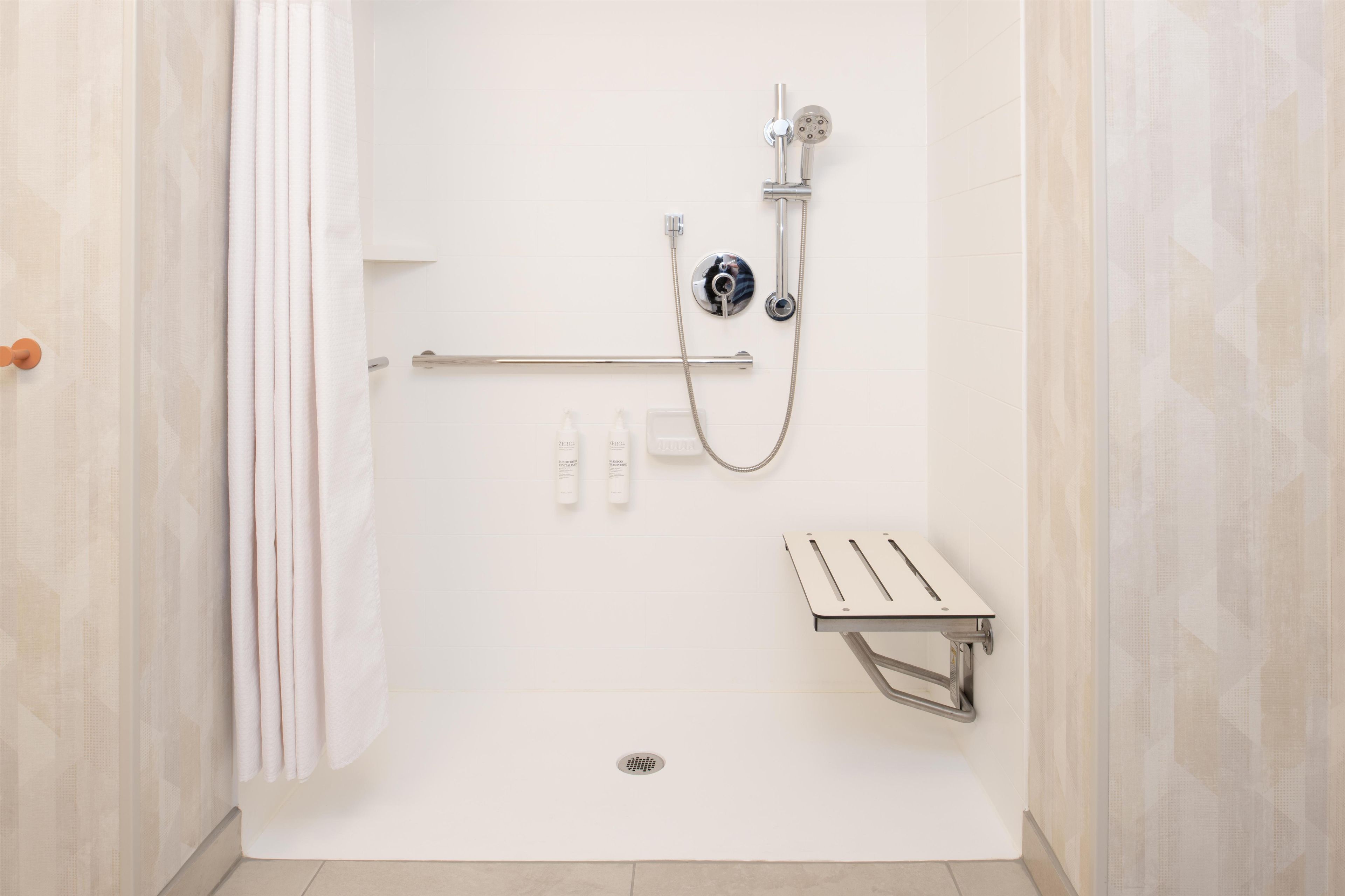 A bathroom with a shower, a handrail, a towel rack, and a toilet.