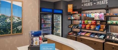A hotel lobby with a counter, a minibar, a refrigerator, and shelves stocked with snacks.