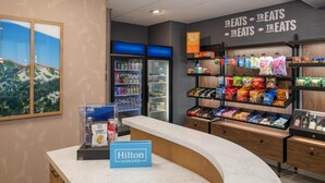 A hotel lobby with a counter, a minibar, a refrigerator, and shelves stocked with snacks.