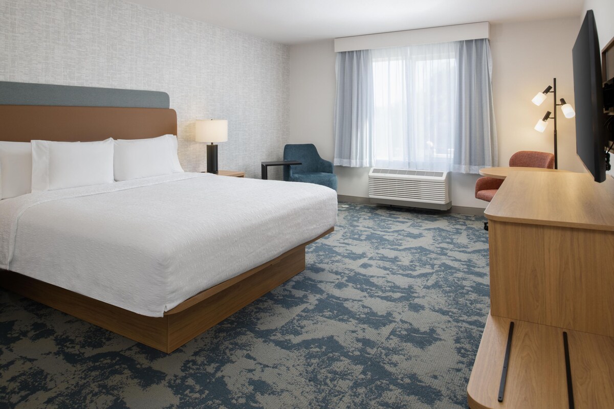 Una habitación de hotel con una cama grande, un escritorio, una silla, un televisor y una ventana con cortinas.
