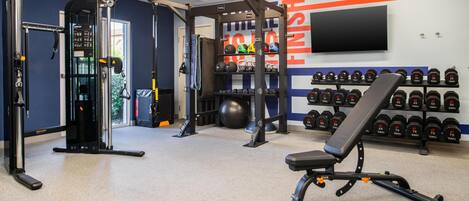 Ein Fitnessraum mit Gewichte, einer Bank und einem an der Wand befestigten Fernseher.