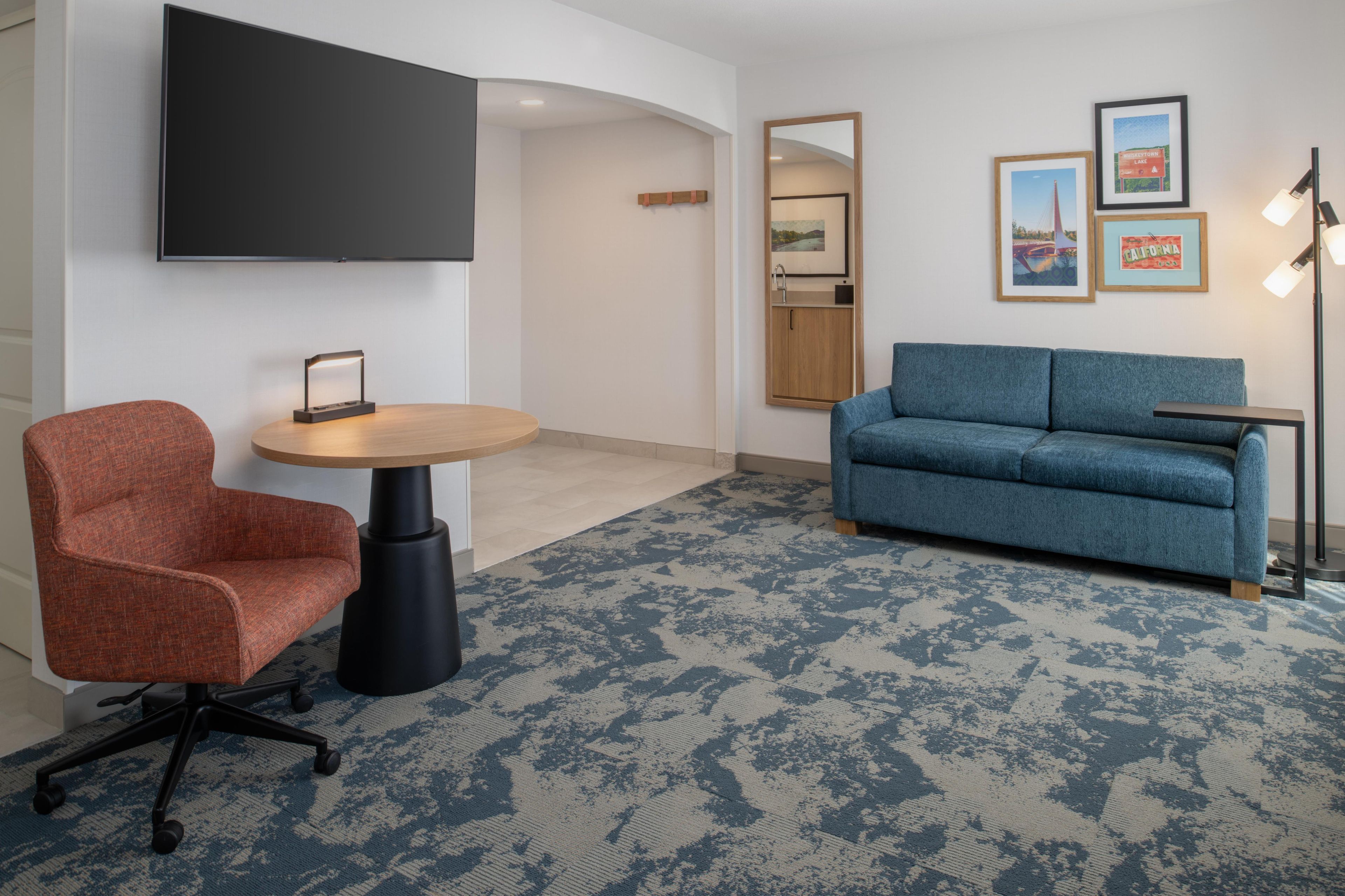 A modern room with a blue sofa, a red chair, a round table, a mounted TV, and framed pictures on the wall.