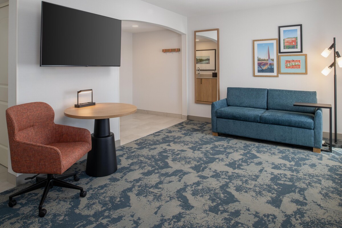 Una habitación moderna con sofá azul, silla roja, mesa redonda, televisor montado y cuadros en la pared.