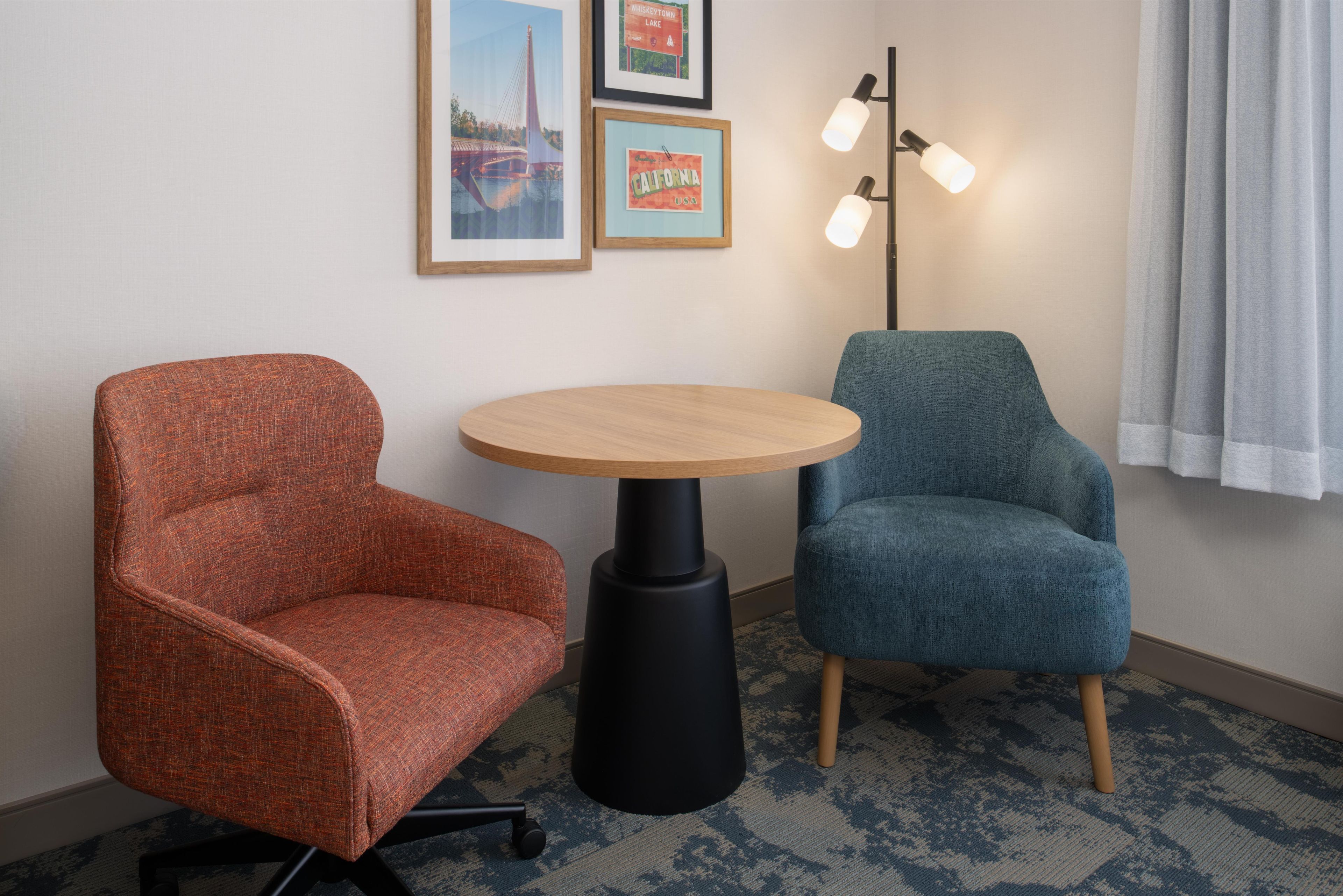 Ein Zimmer mit einem runden Tisch, zwei Stühlen, einer Stehlampe und gerahmten Bildern an der Wand.
