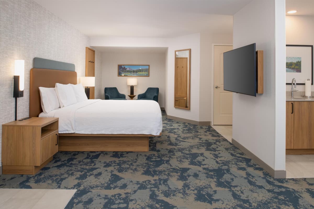A modern hotel room with a bed, bedside tables, a desk, a chair, a TV, and a bathroom.