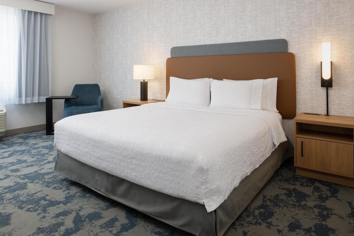A hotel room with a large bed, two bedside tables, a chair, a lamp, and a wall-mounted light fixture.
