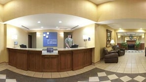 Een hotel receptie met een houten balie, een digitaal scherm en een zithoek met een open haard.