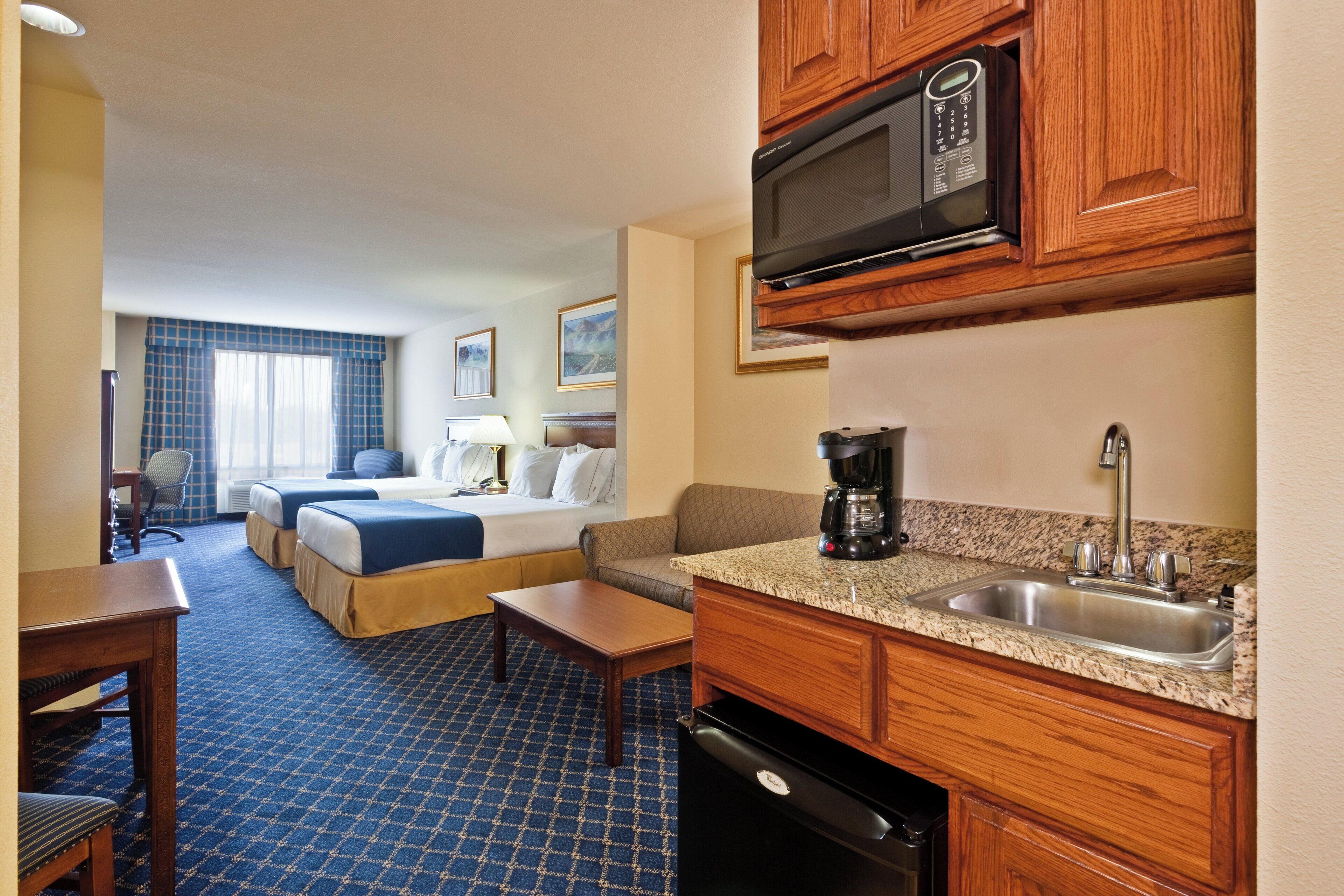 A hotel room with a kitchenette, a bed, a desk, and a chair.