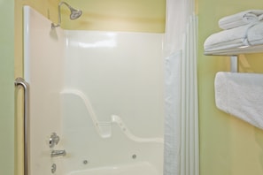 Een badkamer met een witte badkuip, een douche en een handdoekrek met opgevouwen handdoeken.
