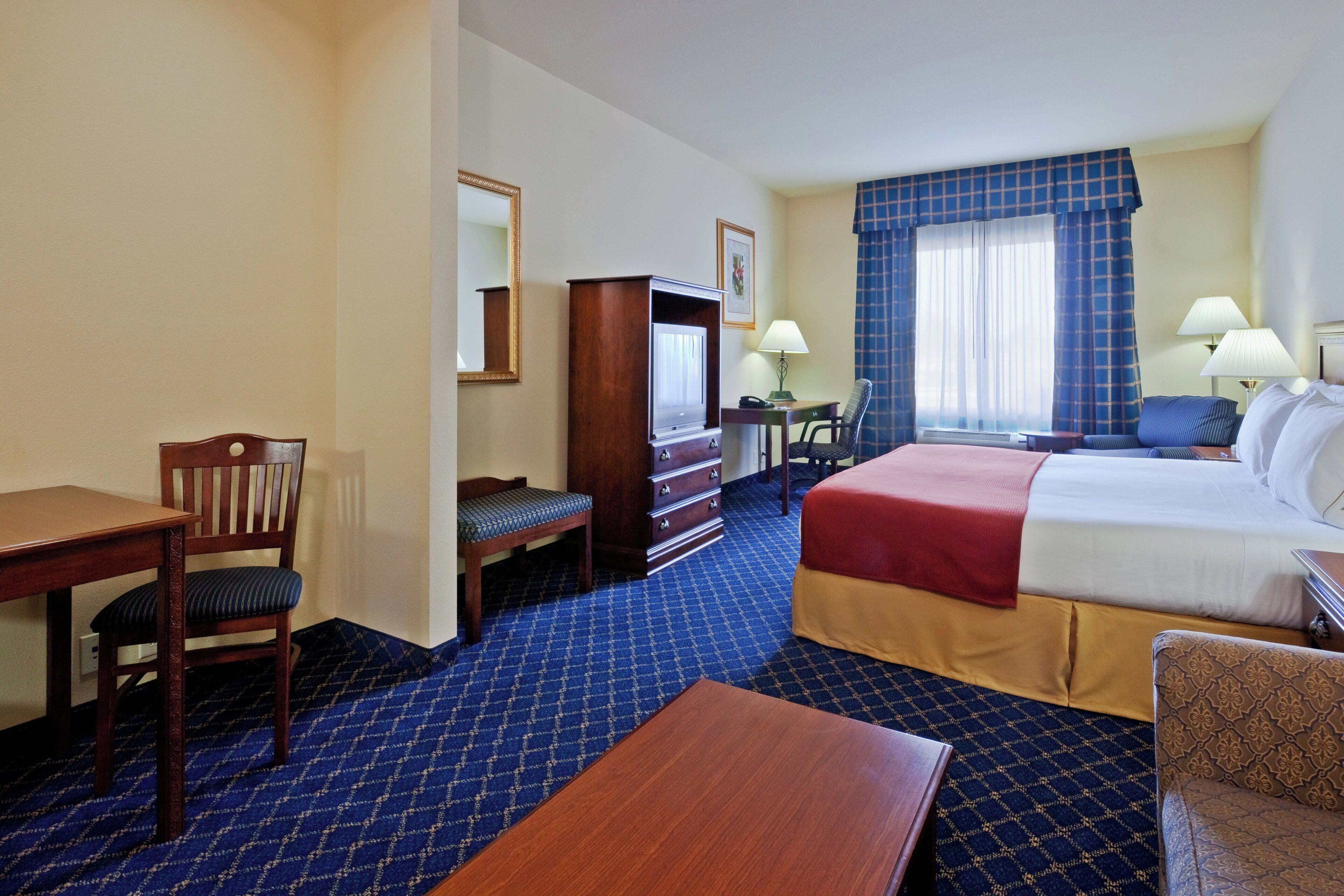 A hotel room with a bed, desk, chair, dresser, and a television.