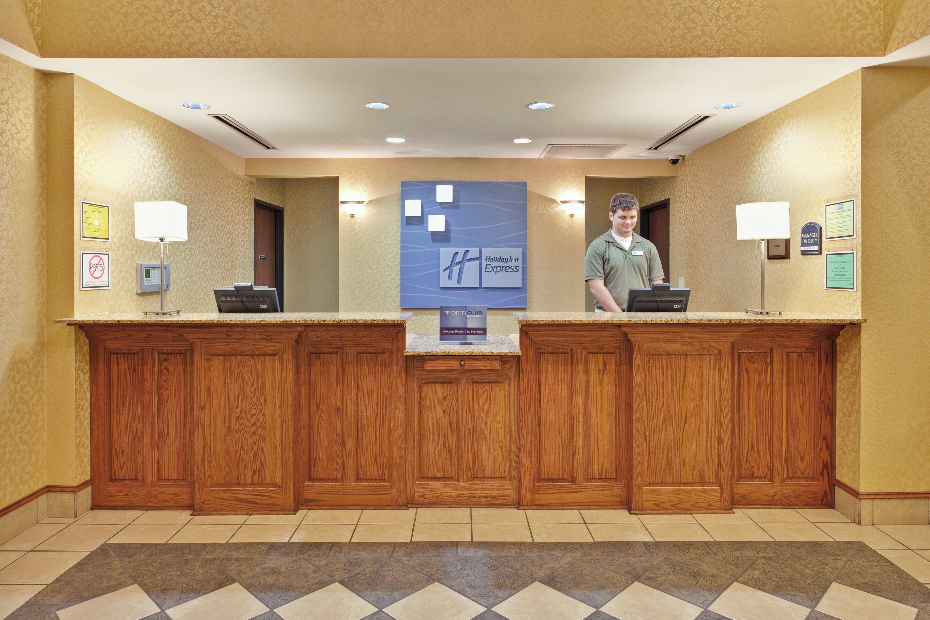 A reception desk with a wooden finish, a blue sign indicating hotel amenities, and a tiled floor with a diamond pattern.