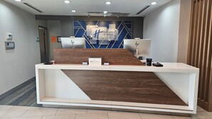 Uma receção de hotel com design moderno, um ecrã digital e um letreiro a indicar 'Holiday Inn Express & Suites'.