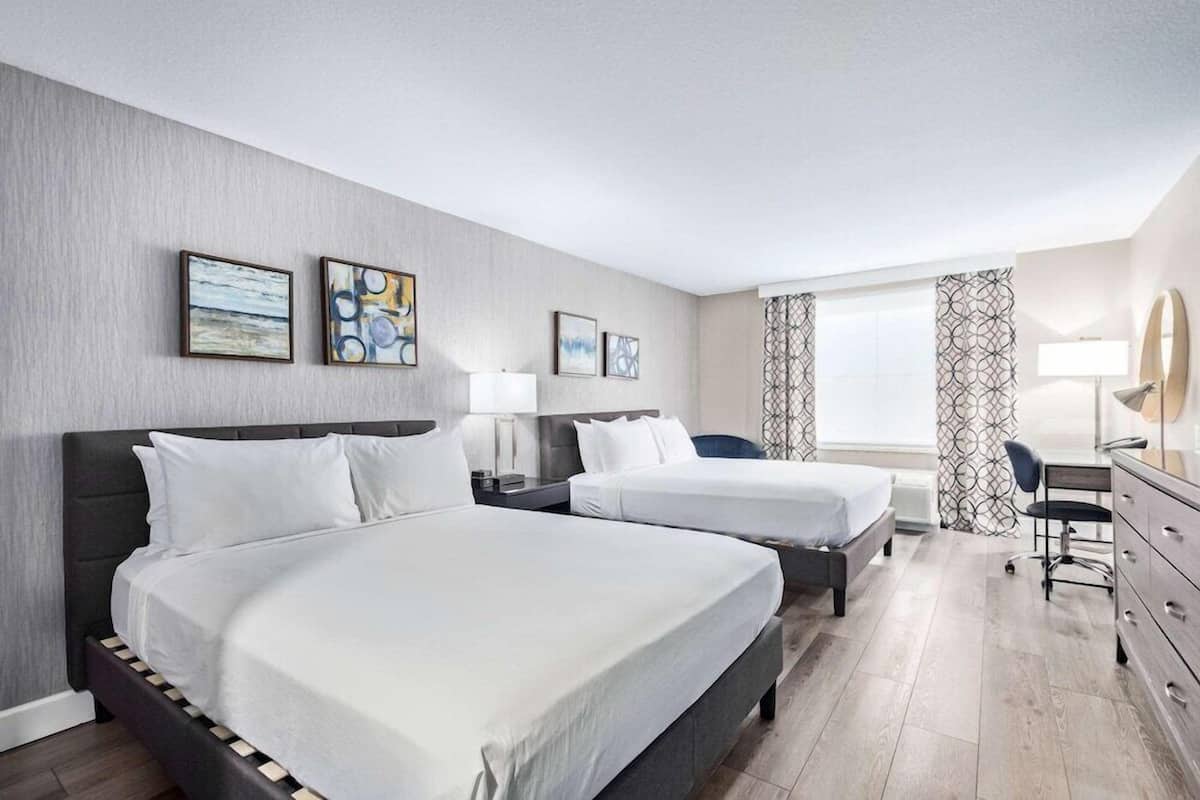 A hotel room with two beds, a desk, a chair, and artwork on the walls.