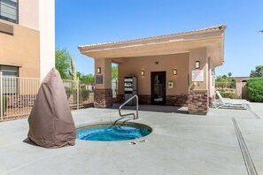 An outdoor swimming pool with a covered area, a lifeguard chair, and a sign indicating an emergency phone switch. - Fountain Park Hotel, BW Signature Collection (Fountain Hills)