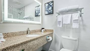 A bathroom with a granite countertop sink, a mirror, a toilet, and a towel rack with multiple towels.