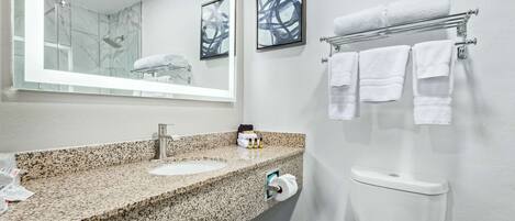 A bathroom with a granite countertop sink, a mirror, a toilet, and a towel rack with multiple towels.