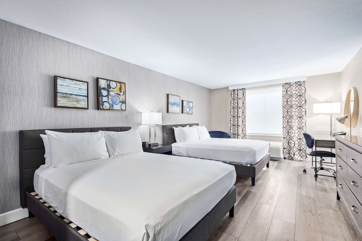 A hotel room with two beds, a desk, a chair, and artwork on the walls.