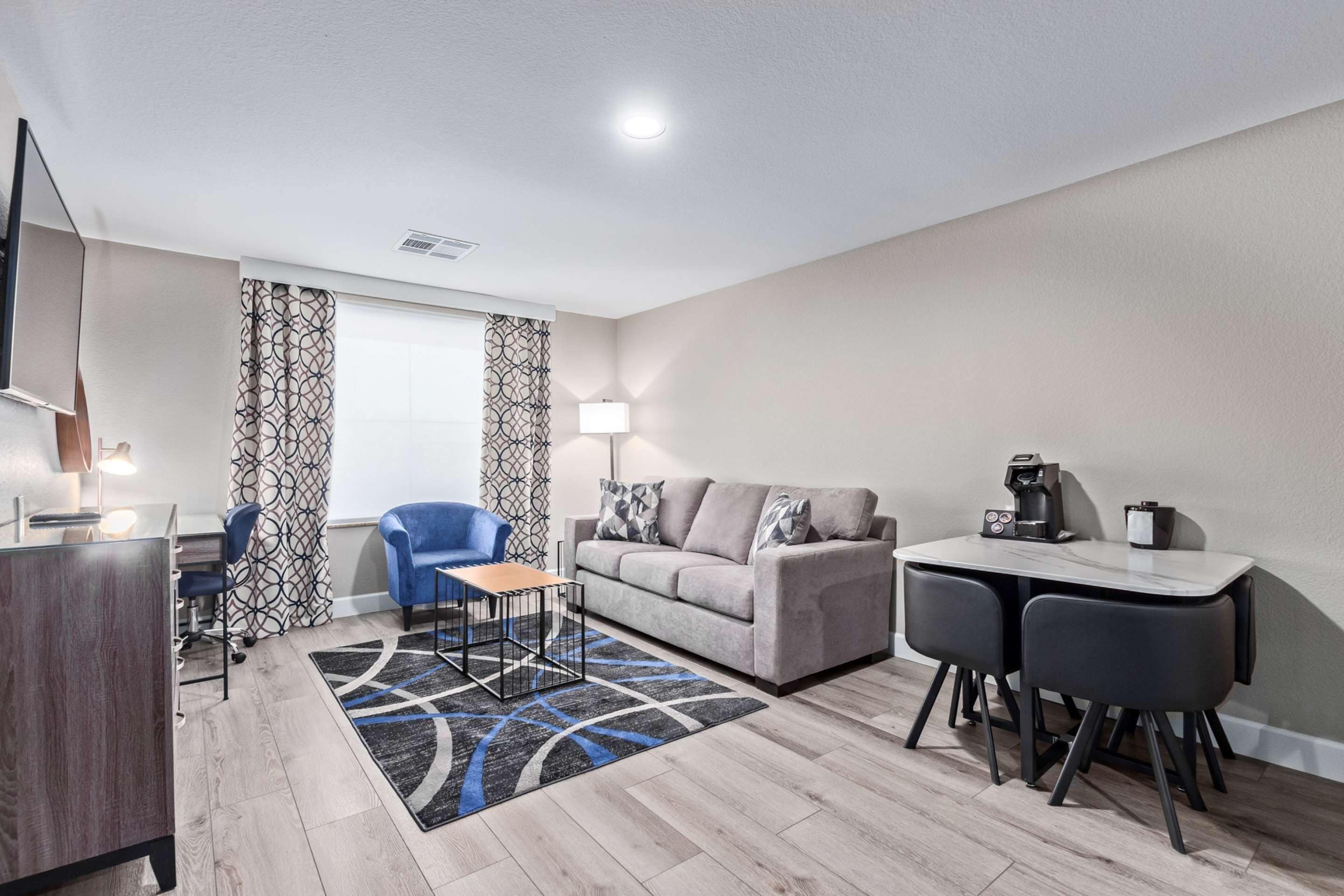 A modern living room with a sofa, two chairs, a coffee table, a TV, and a desk with a lamp.