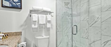 A bathroom with a toilet, a glass shower enclosure, and a marble-tiled wall.