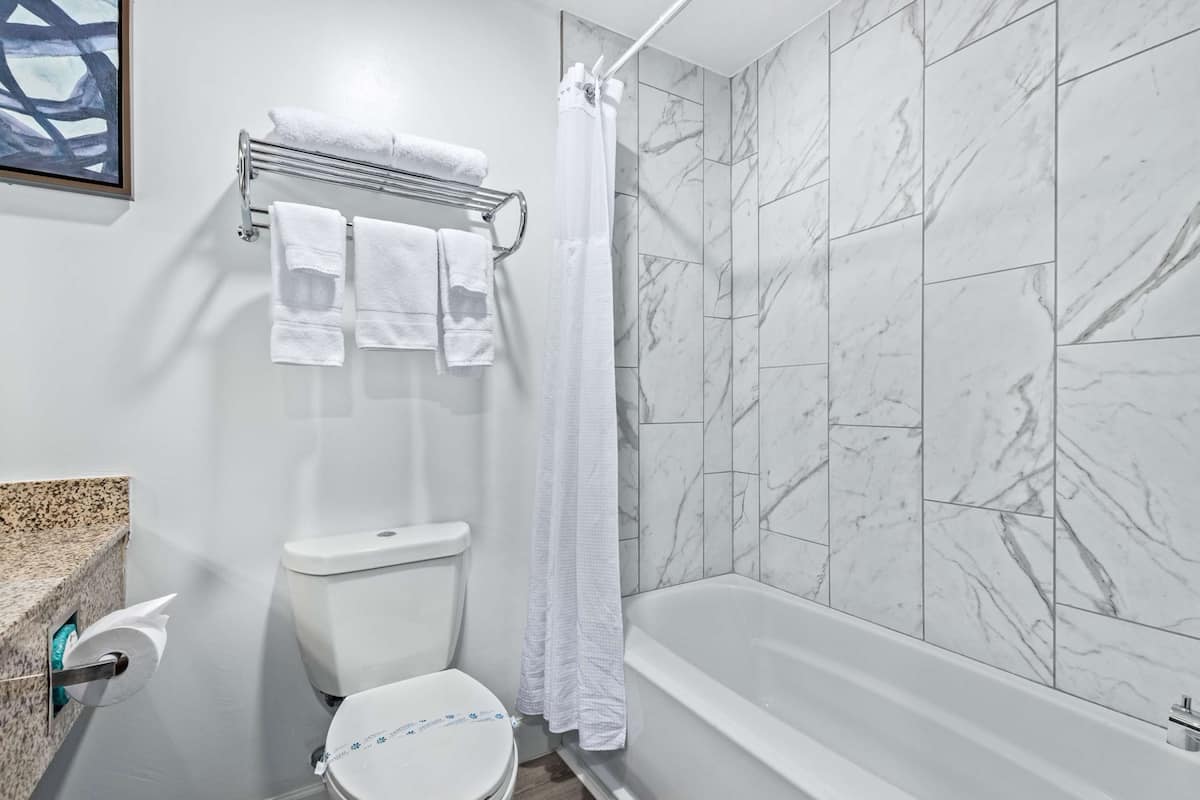 A bathroom with a toilet, a towel rack with towels, a shower curtain, and a bathtub with marble tiles.