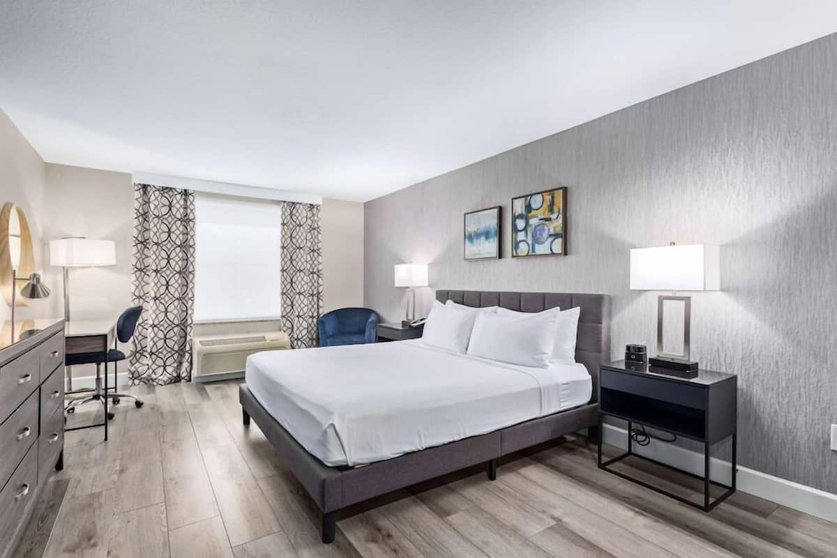 A hotel room with a bed, desk, chair, and artwork on the wall.