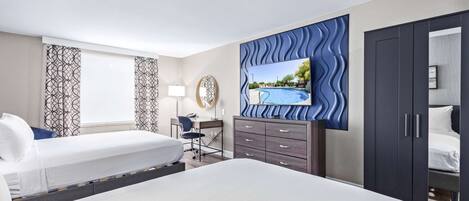 Une chambre d’hôtel avec deux lits, un bureau, une chaise, un téléviseur fixé au mur bleu à texture, et une armoire.