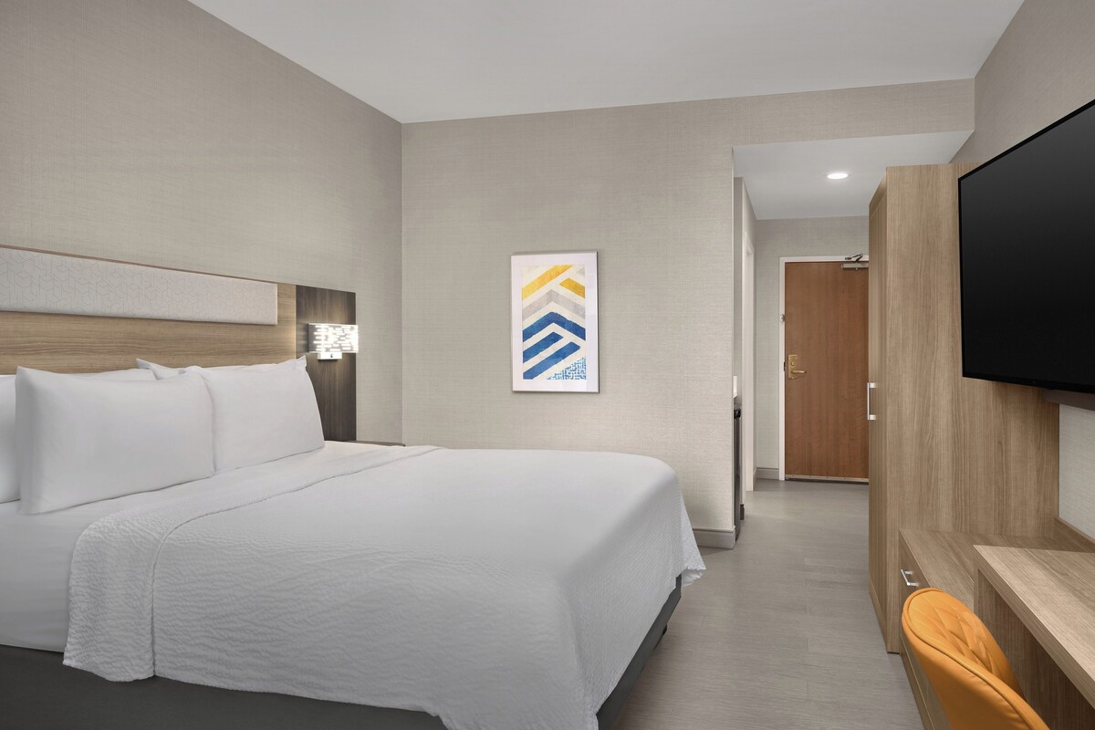 Ein Hotelzimmer mit einem Bett, einem an der Wand montierten Fernseher und einer Tür zu einem anderen Raum.