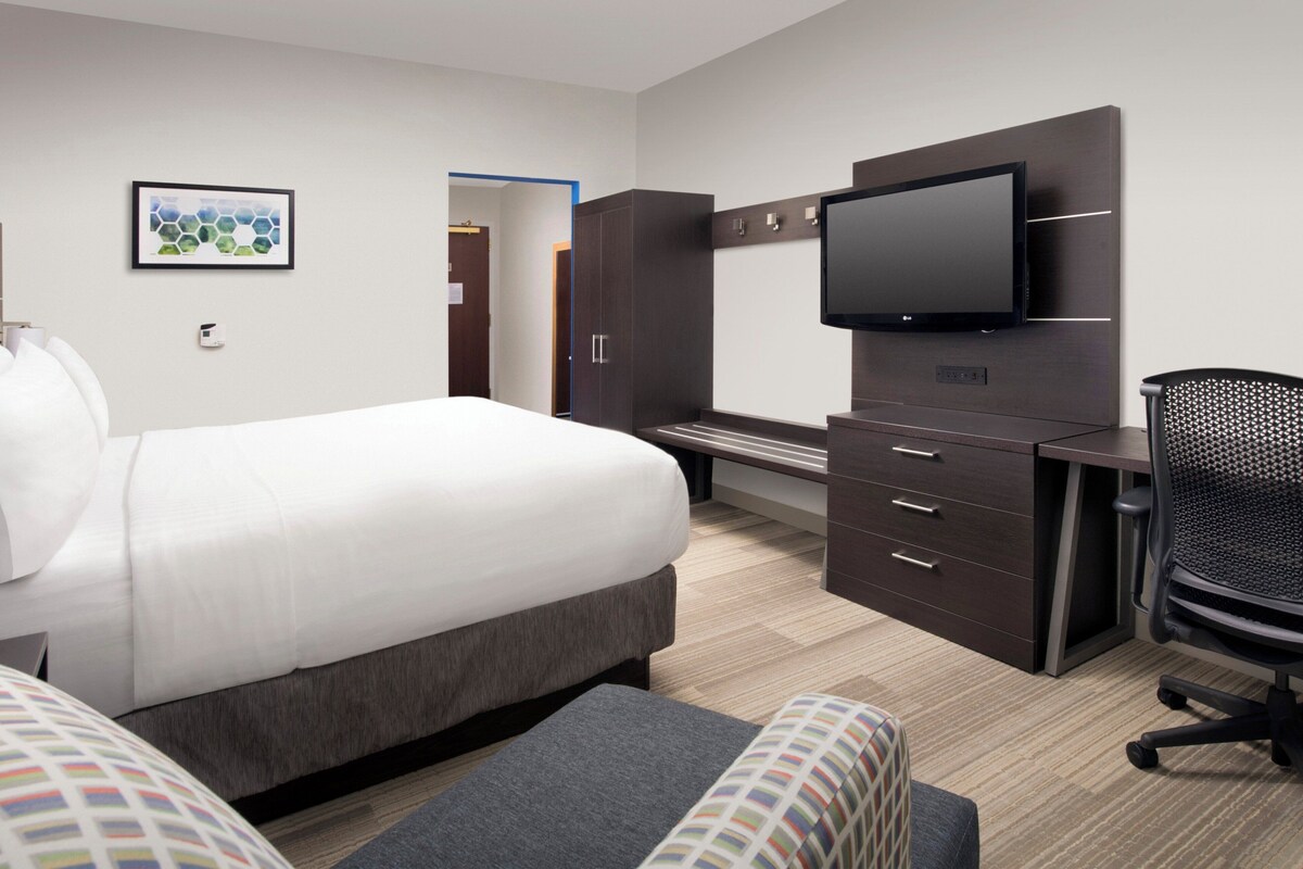 Une chambre d’hôtel avec un grand lit, un bureau doté d’un téléviseur à écran plat, une chaise et une armoire.