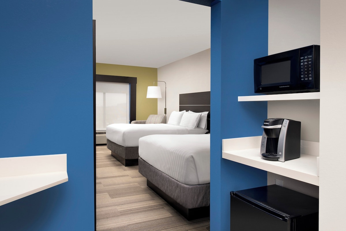 A hotel room with two beds, a microwave, a coffee maker, and a small refrigerator.