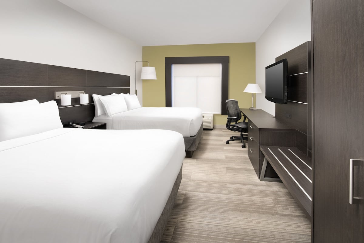 A hotel room with two beds, a TV, a desk, and a chair.