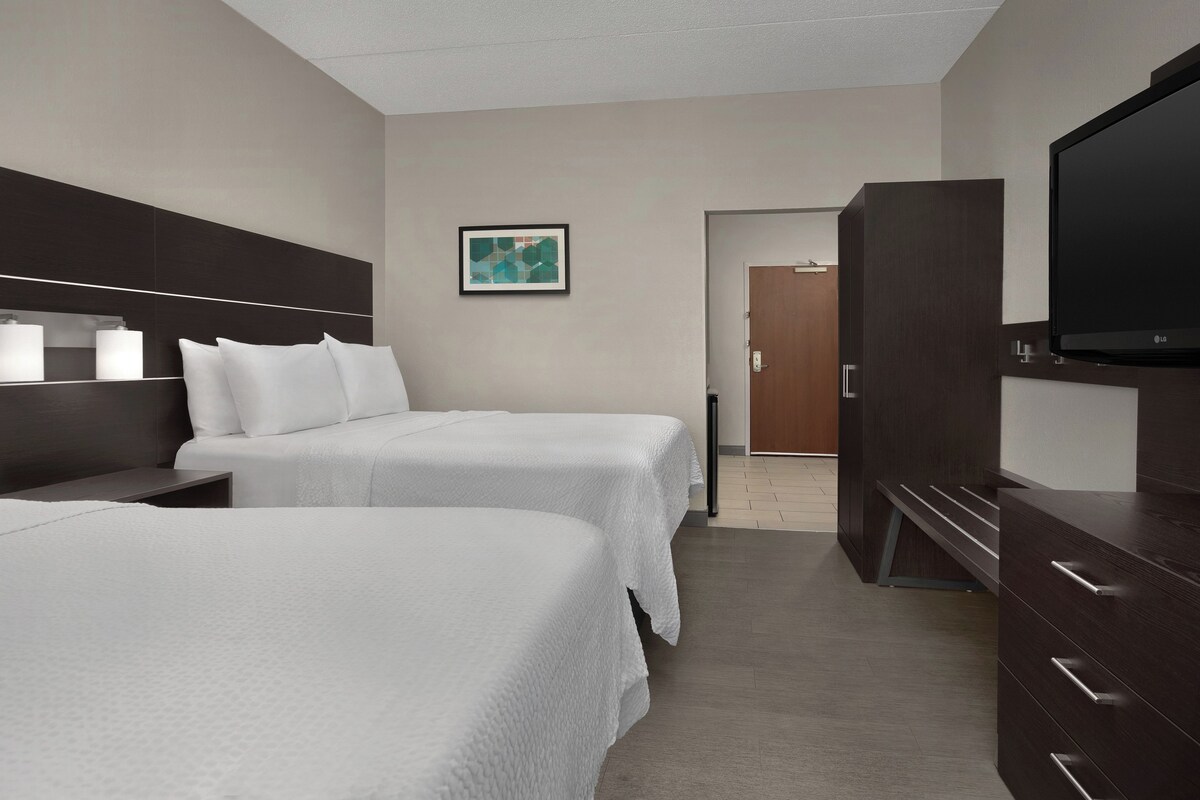 Ein Hotelzimmer mit zwei Betten, einem Fernseher, einem Schrank und einem Bild an der Wand.
