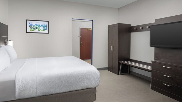 Una habitación de hotel con cama, televisor, armario y una puerta que da a otra habitación.