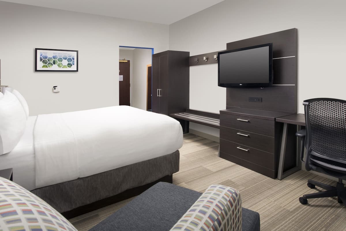 A hotel room with a large bed, a desk with a flat-screen TV, a chair, and a wardrobe.
