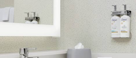 Un baño con lavamanos blanco, espejo, toalla, dispensador de jabón y caja de pañuelos.