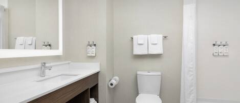 Un baño moderno con lavamanos, espejo, inodoro y cortina de ducha blancos.